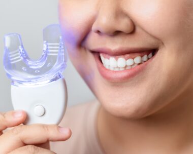person smiling and holding a teeth whitening kit and LED light