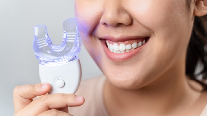 person smiling and holding a teeth whitening kit and LED light