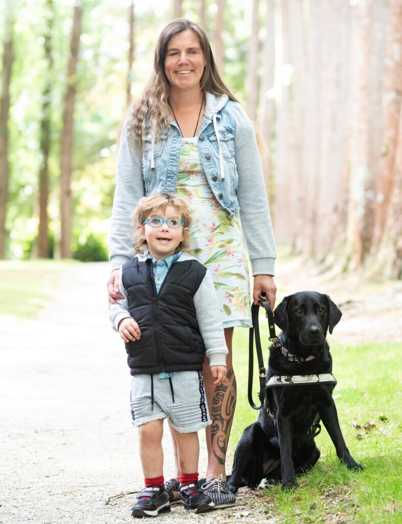 Hannah stands behind son, Max and her black guide dog, Dara.