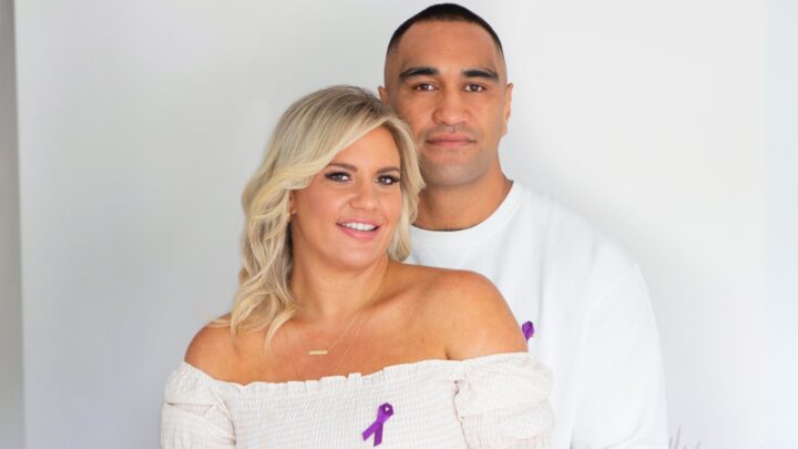 Marata Niukore with his arms around his partner, Nikki Johns, both wearing white with a purple ribbon pinned to their chests