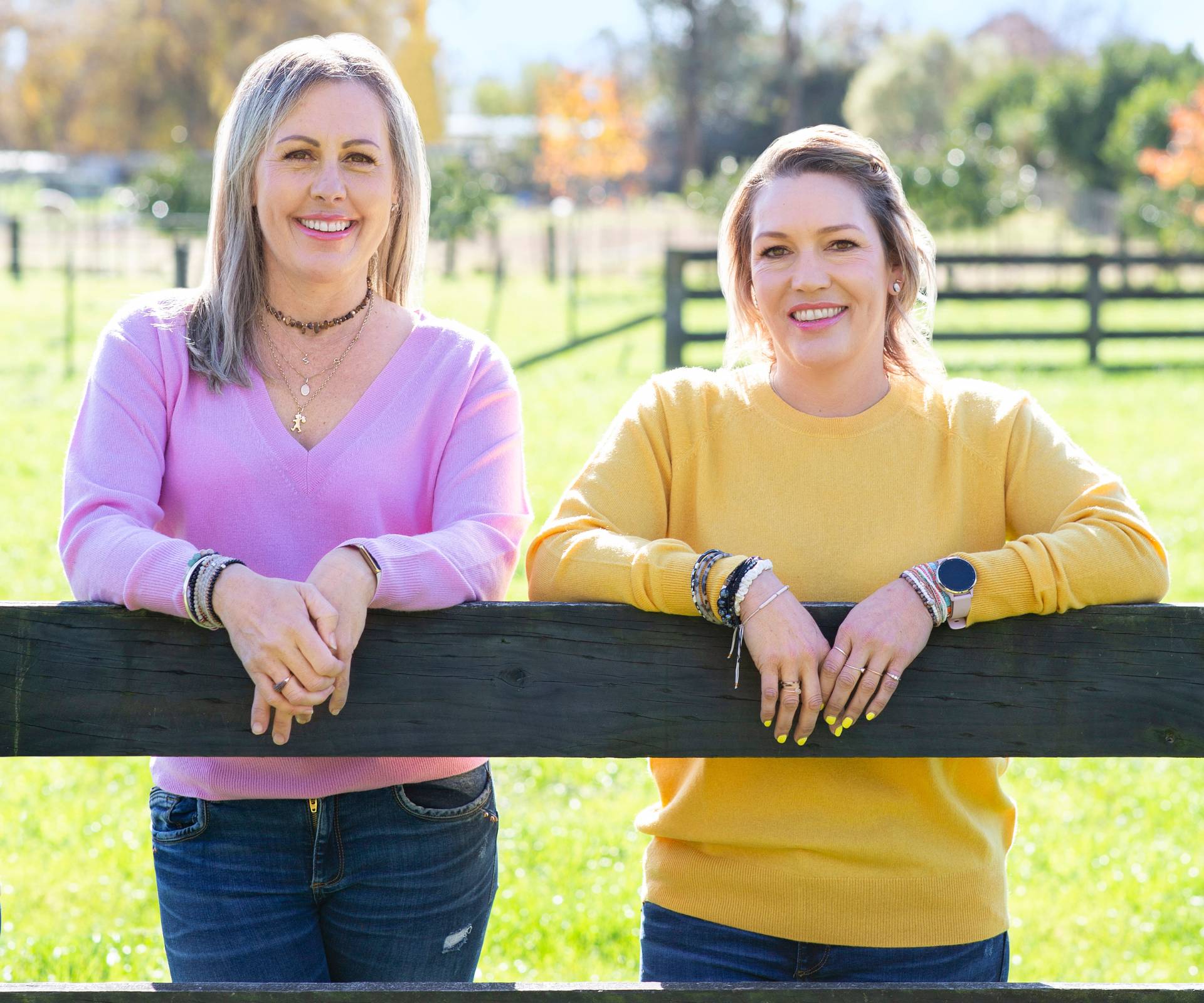 Jackie and Becki leaning on a fence, smiling at the camera