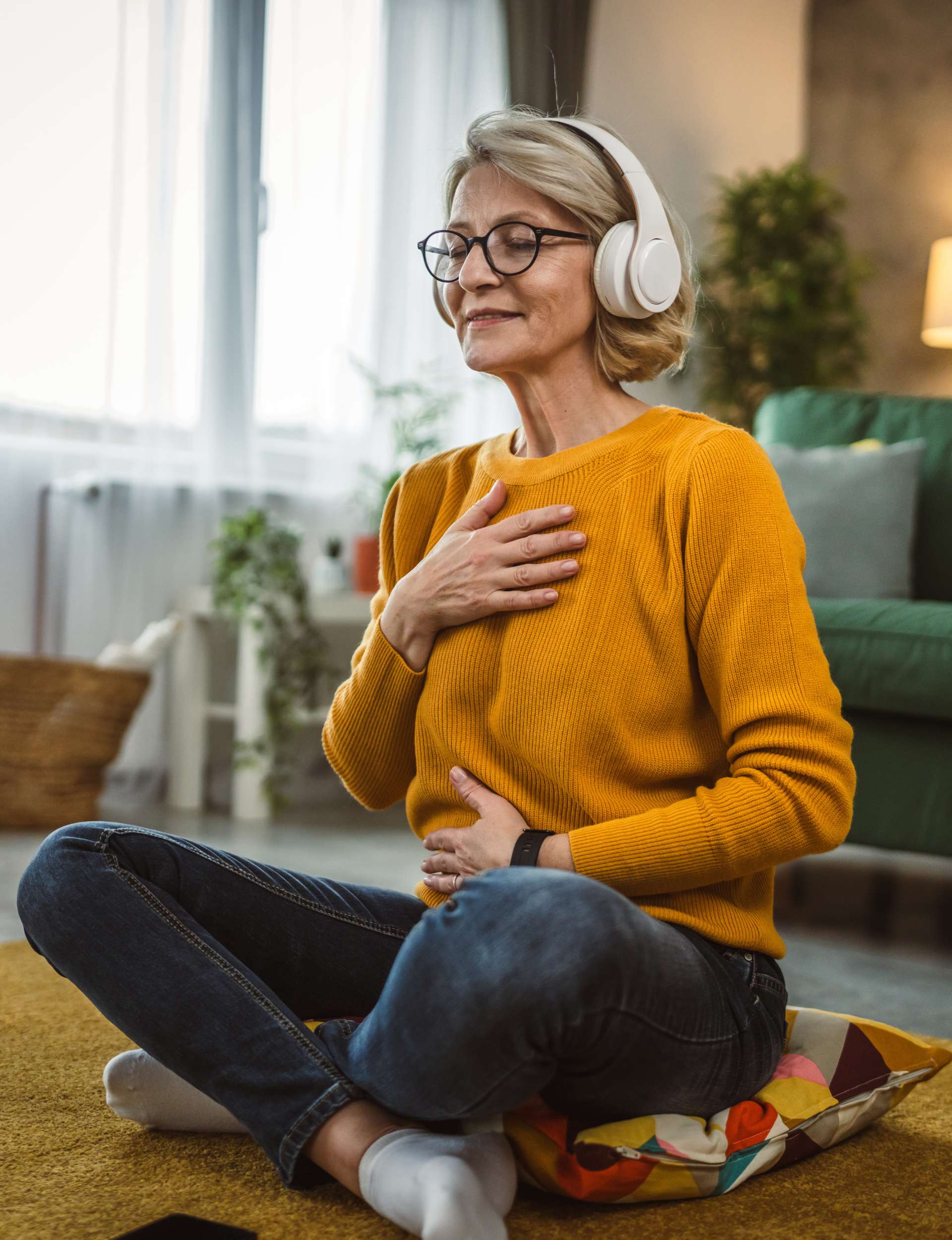 Woman sitting cross-legged with her hands on her diaphragm wearing headphones