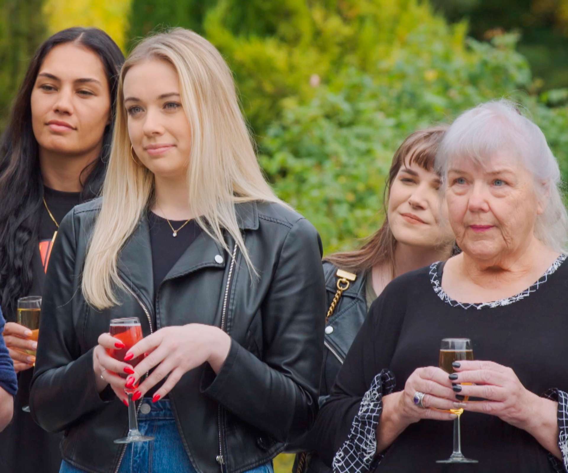 Jackie holding a champagne flute while standing beside other Traitors stars