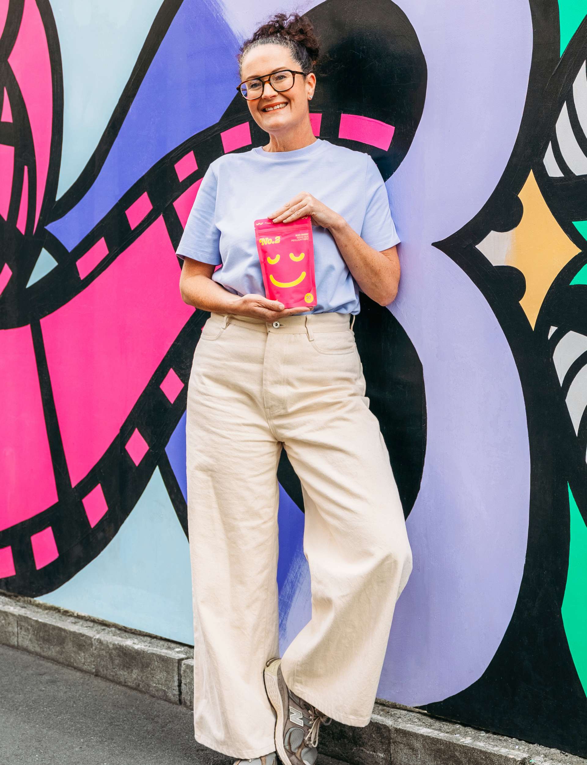 Alice holding up her product in front of a graffitied wall