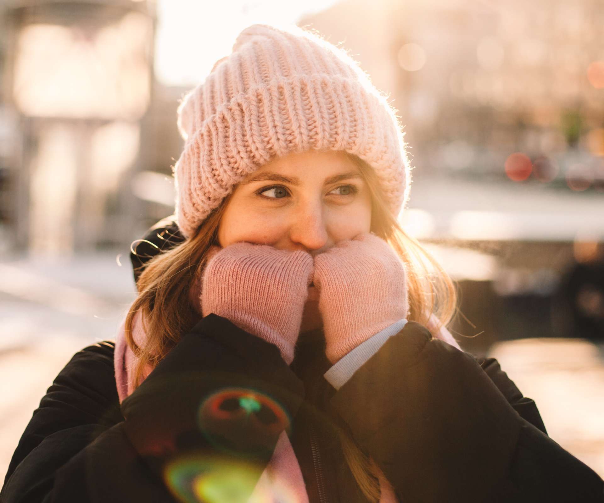 Young woman warming her hands while standing on the street in city during cold weather in winter