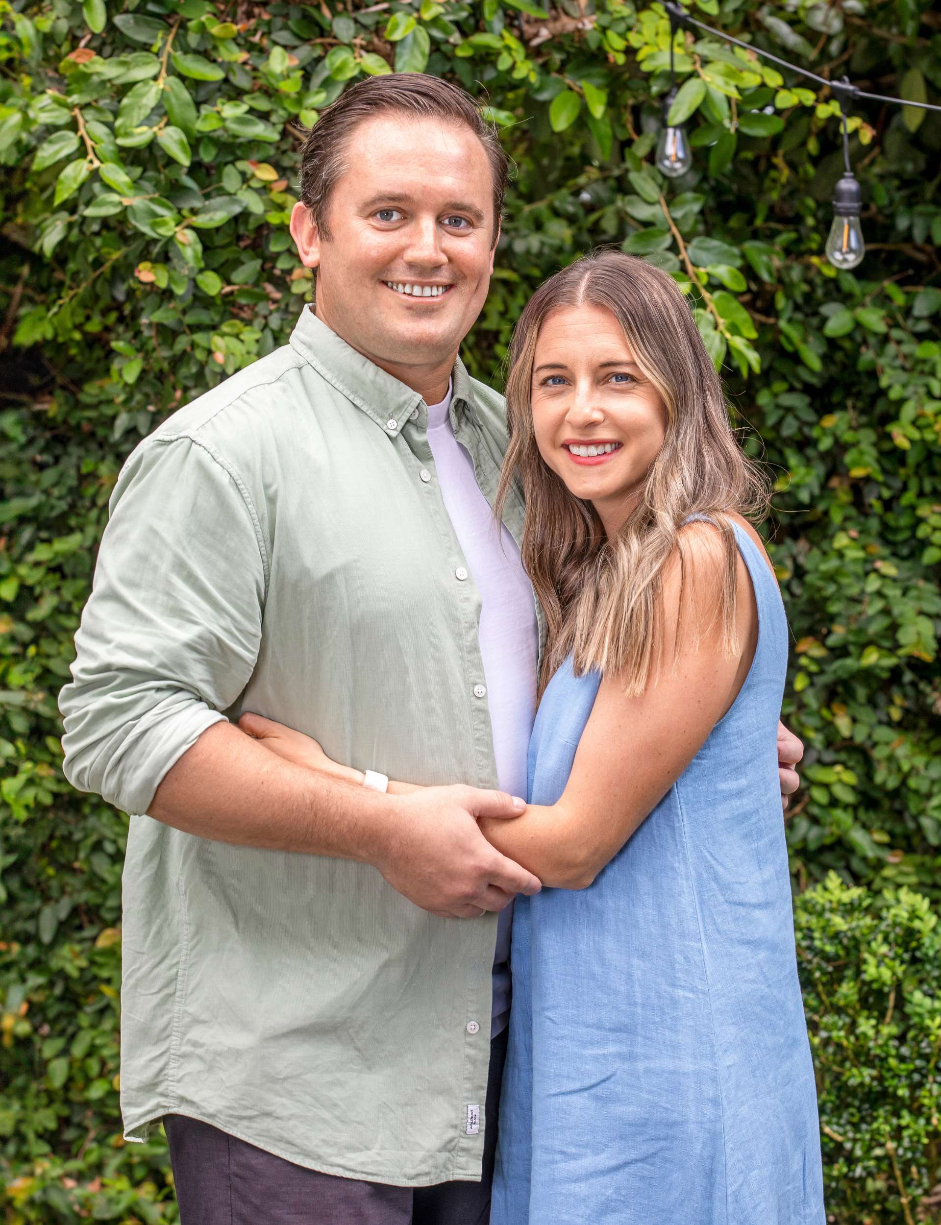 Kiwi couple Emma and Travis hugging in front of a hedge