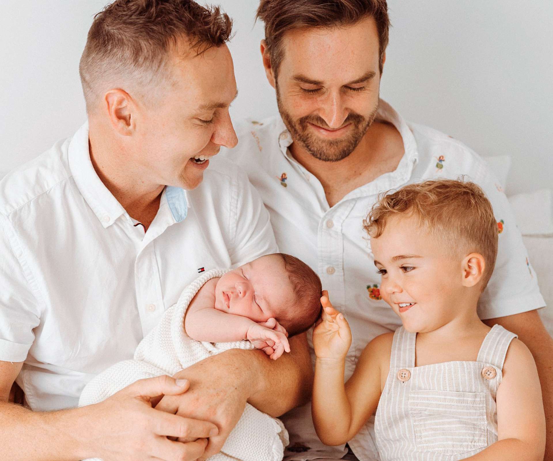 Kiwi couple Mark and Christian and their son holding their baby they got through surrogacy