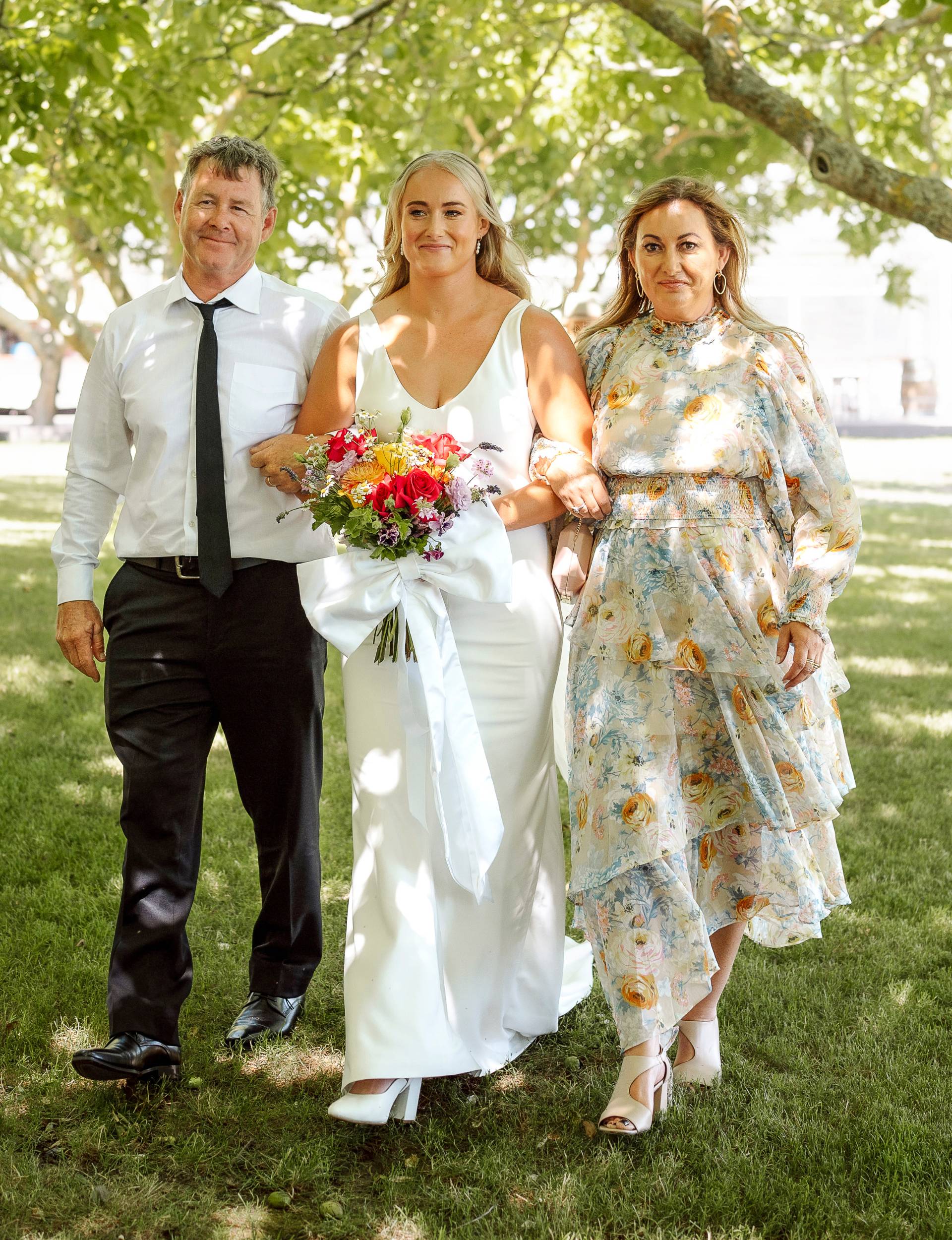 Grace Steinmetz walking up the aisle with her parents linked under each arm 