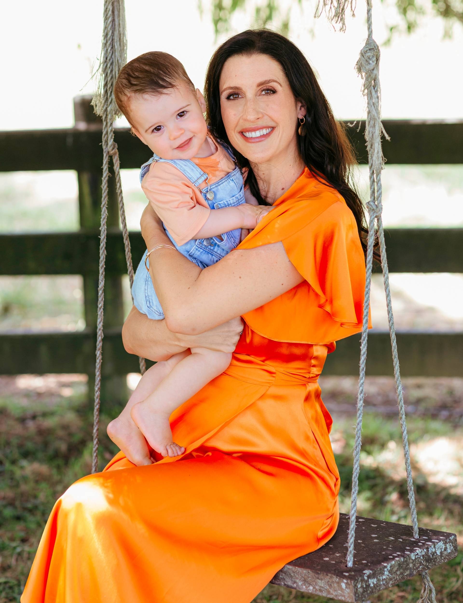 Nadine Higgins sitting on a tree swing holding baby Frankie