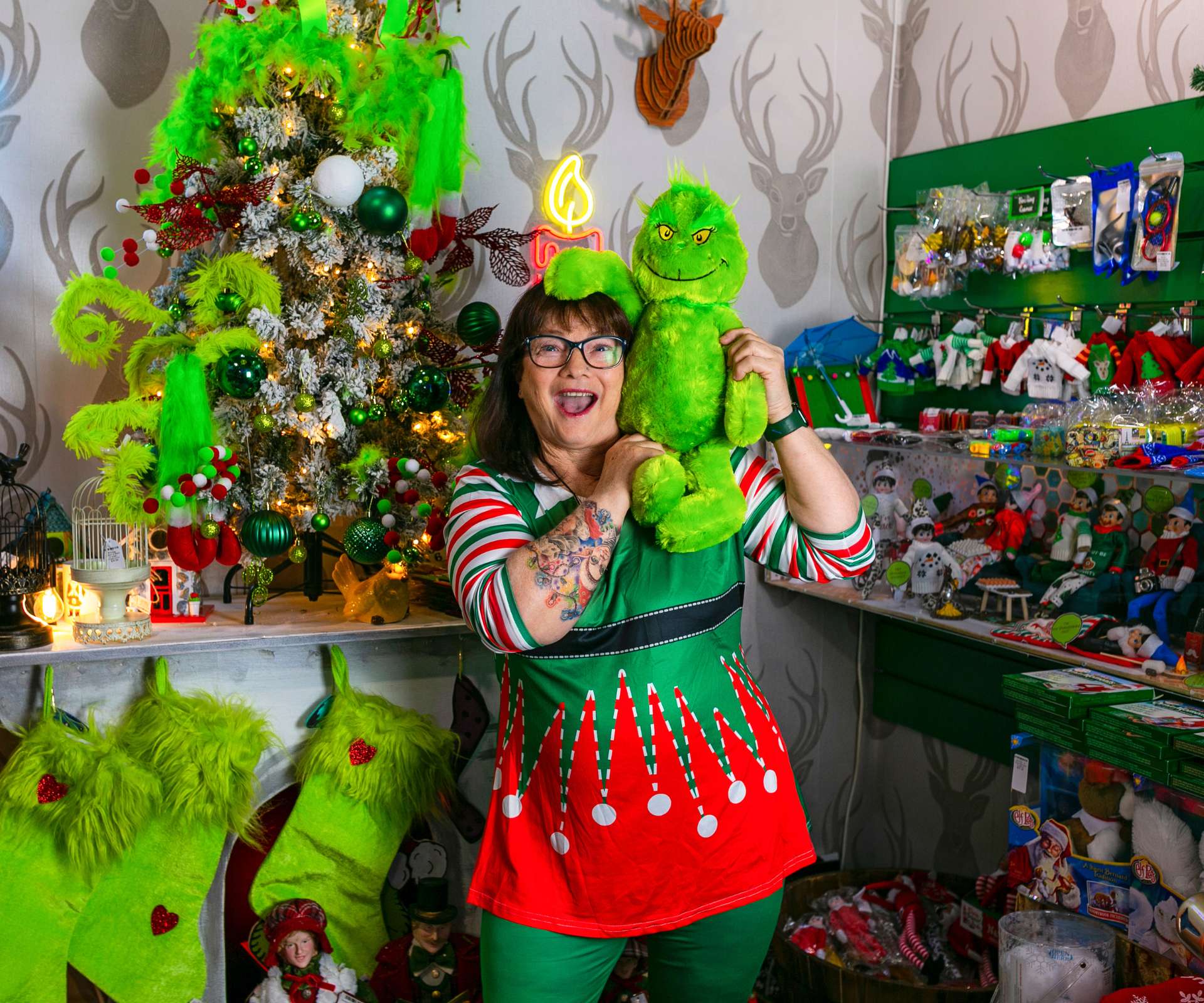 woman dressed as a Christmas elf holding a toy that looks like the Grinch