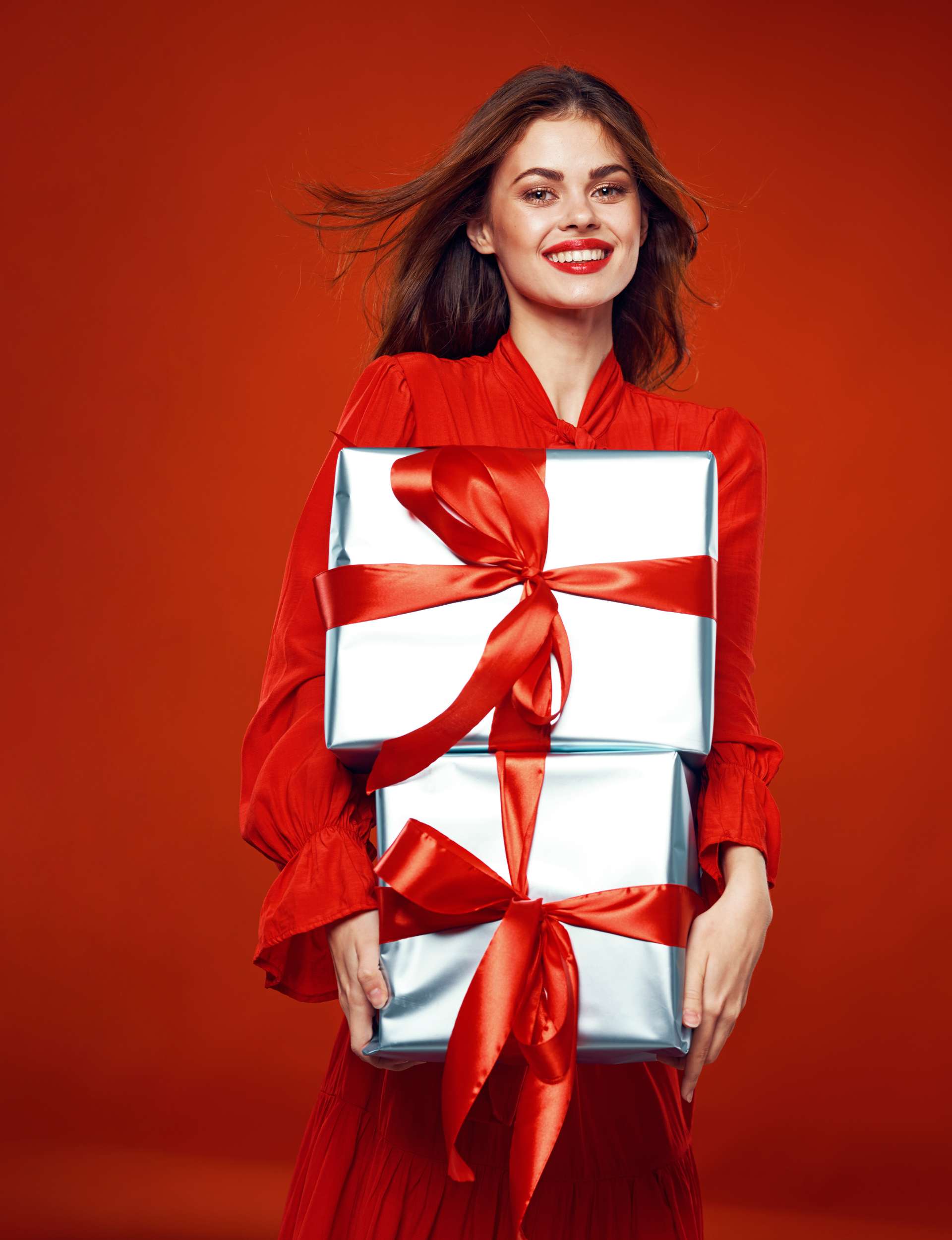 Woman holding silver presents with a red bow wearing red clothes with red lipstick and a red background