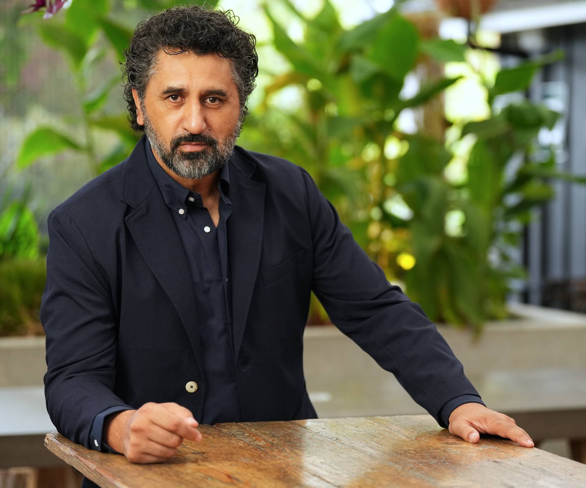 Cliff Curtis leaning on a wooden table