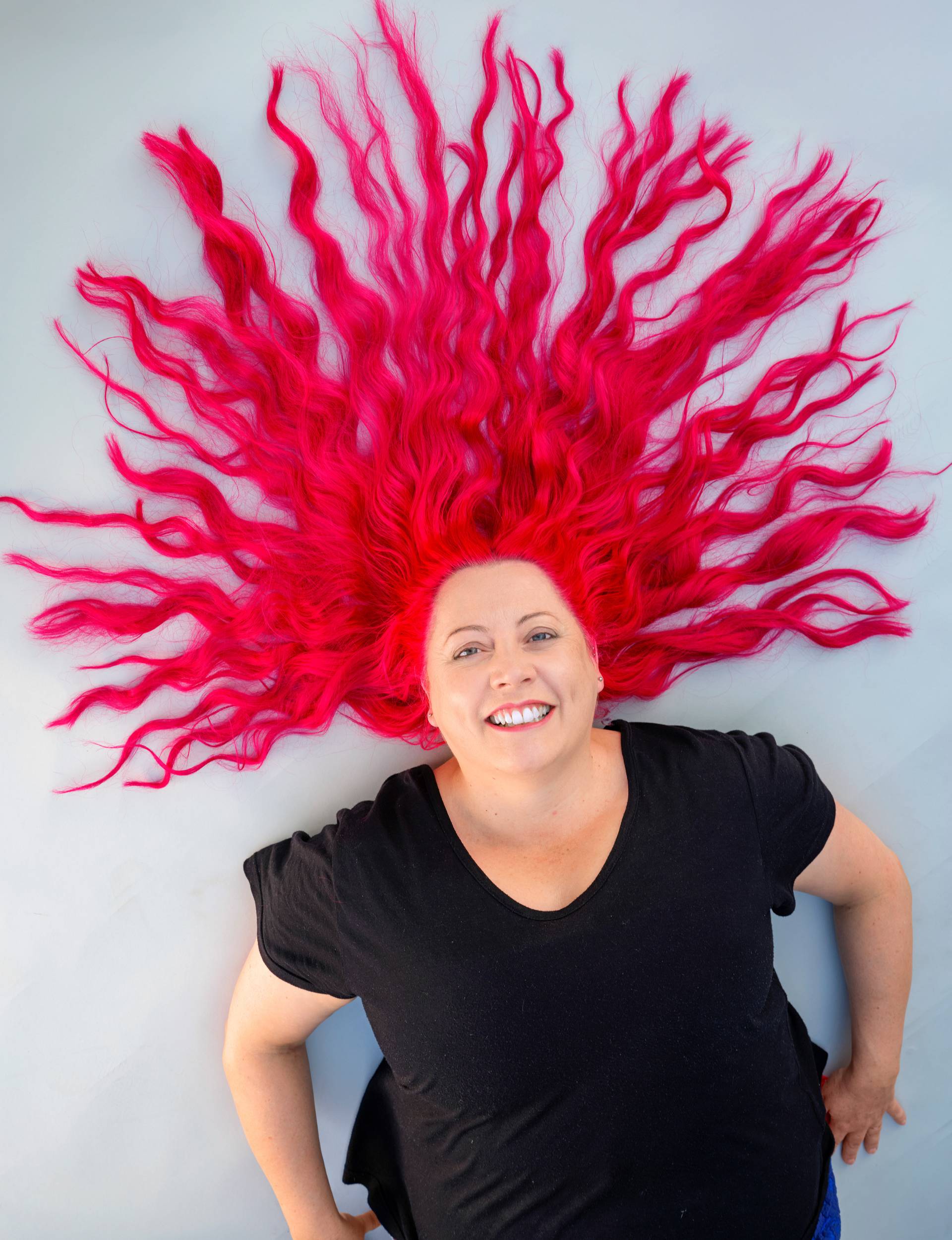Dr Siouxsie laying on a white surface with her red hair spread out
