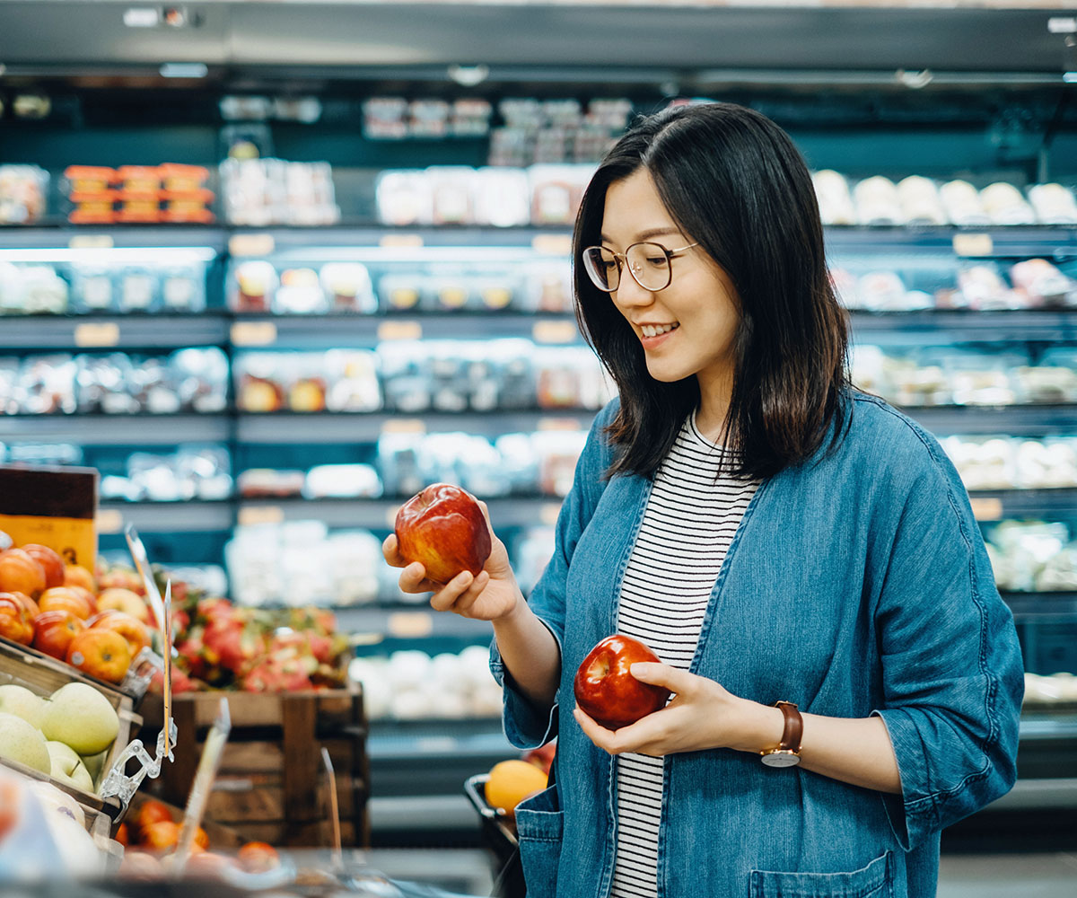 asian woman with glasses choosing apples at the supermarket