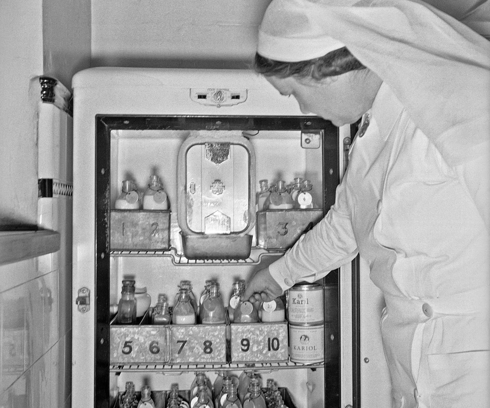 A nurse reaches inside a fridge for bottles of infant formula at the Karitane Hospital, Christchurch, 1943.